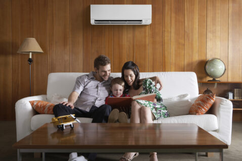 Parents on couch reading with young child with mini split heat pump on the wall behind.